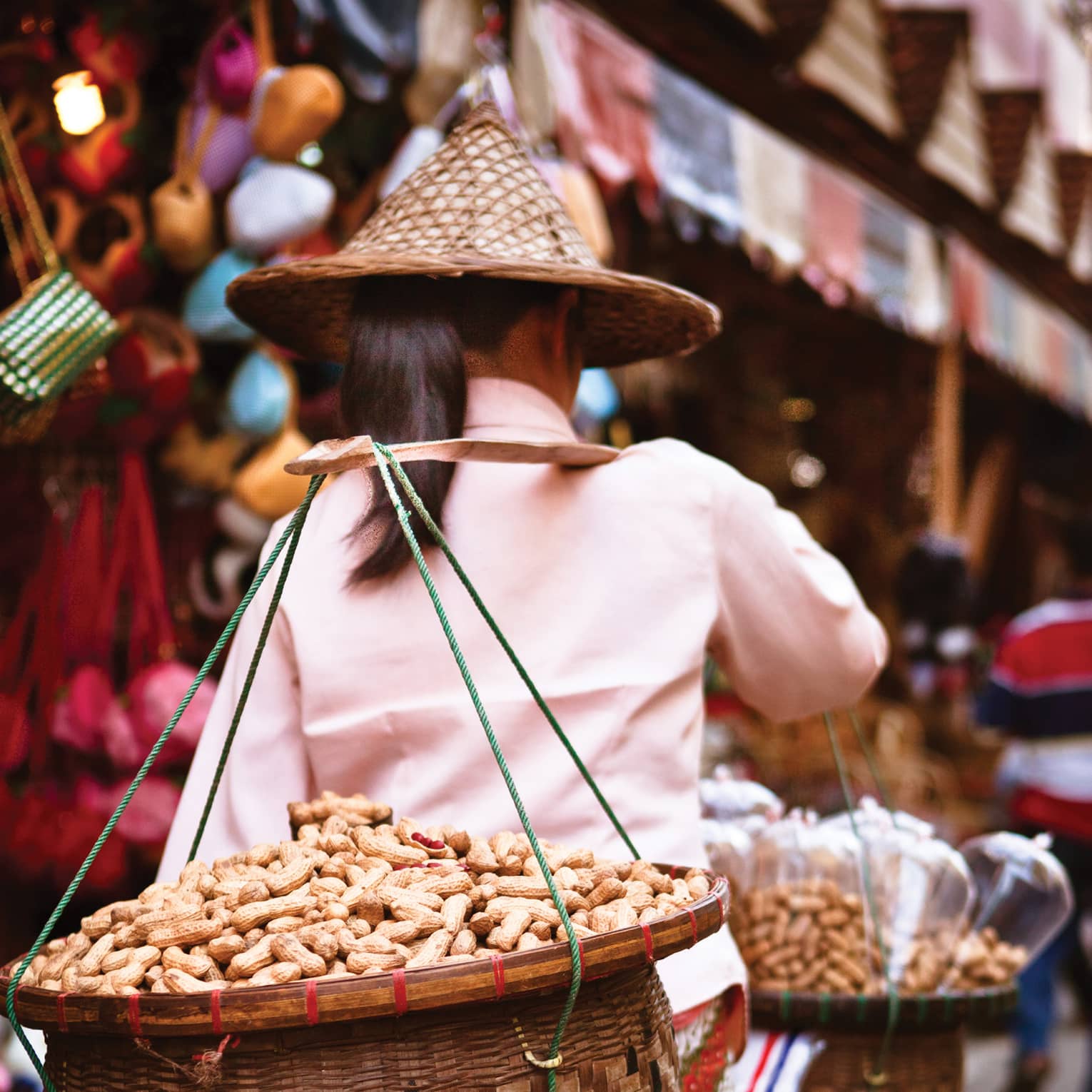 Street vendor with a conical hat carrying goods on a shoulder pole in a busy market