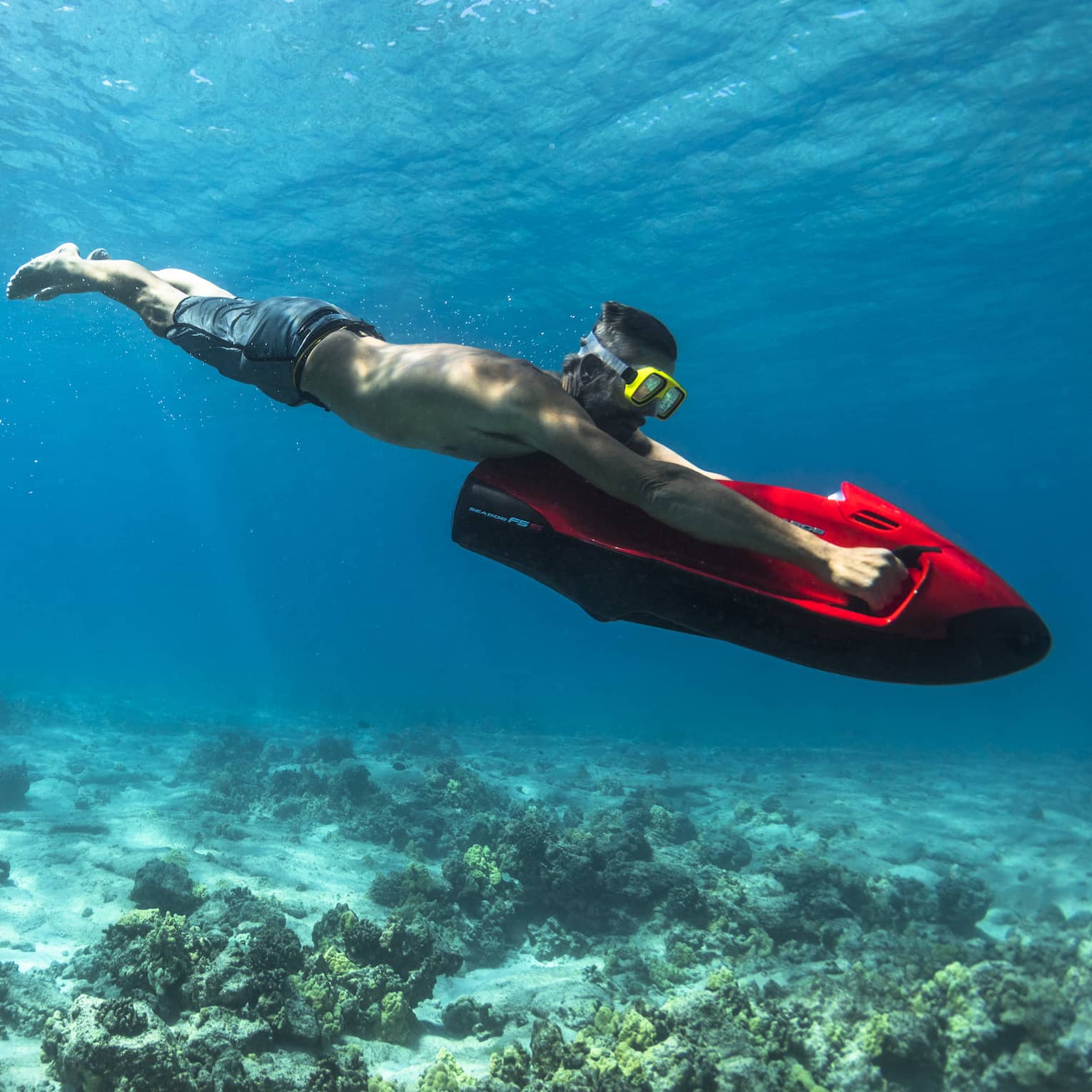 Man dives in ocean over coral, holding red inflatable board