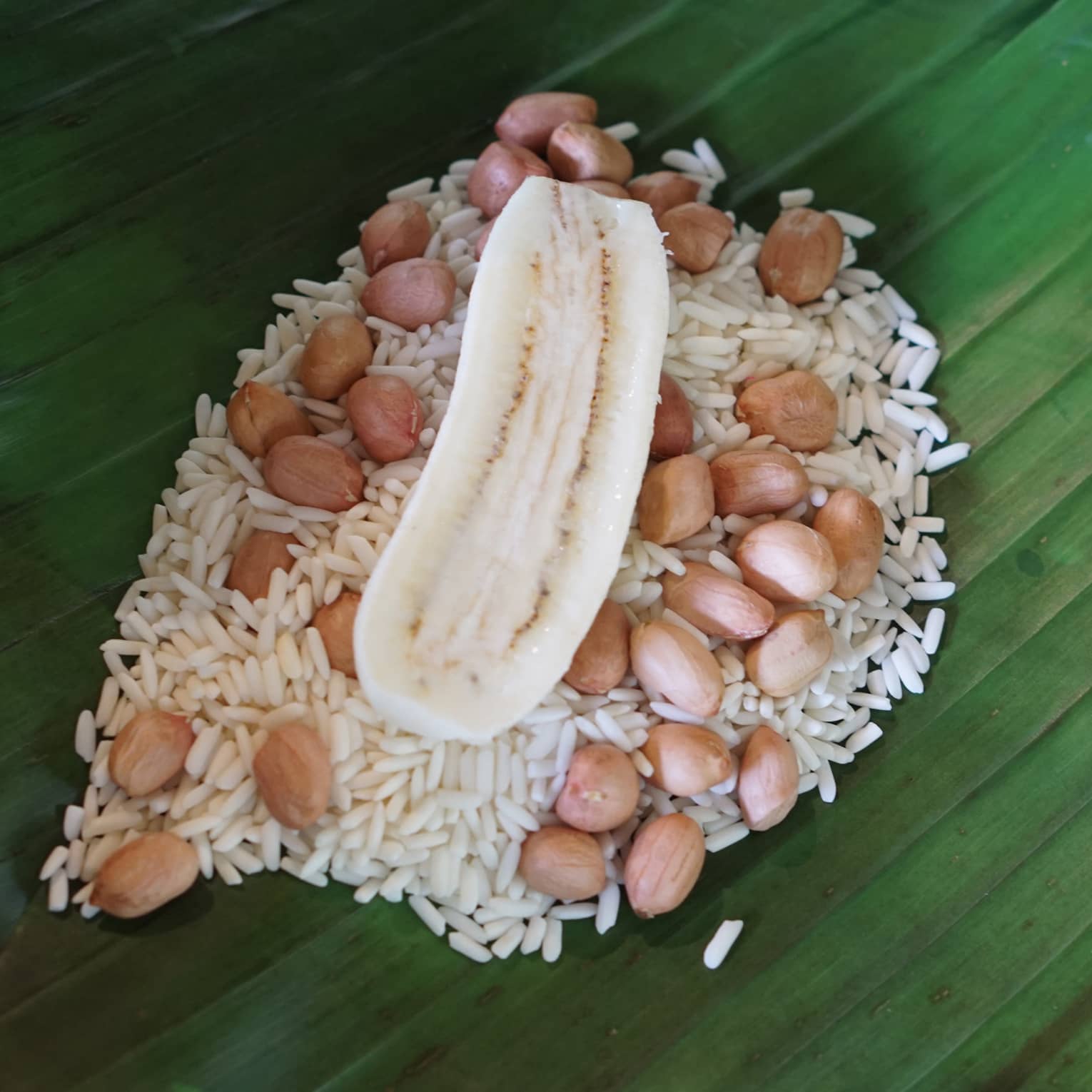Uncooked banana, peanuts and sticky rice placed on a green banana leaf for wrapping