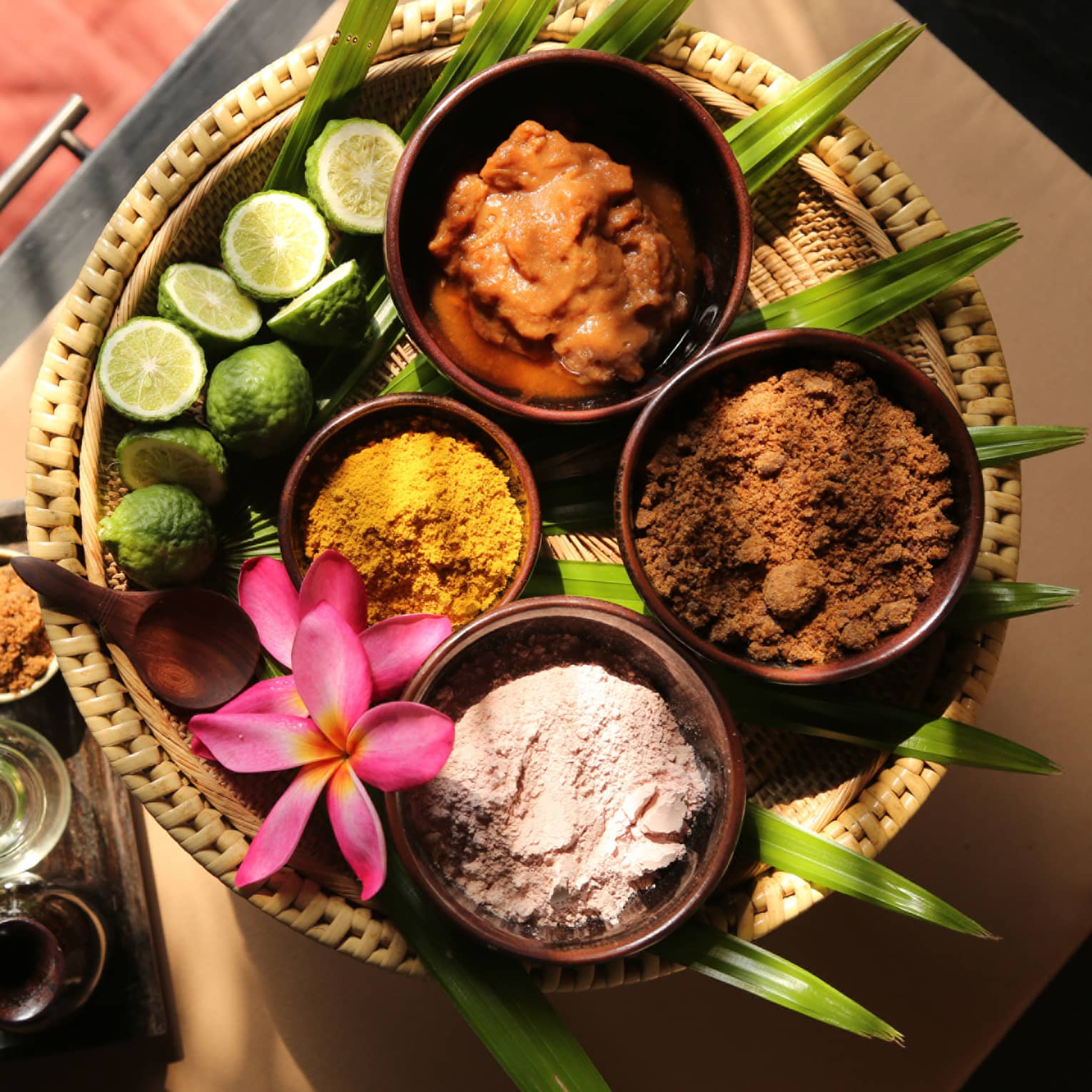 Assorted natural spa ingredients in bowls with lime, assorted spices and flower on a woven tray