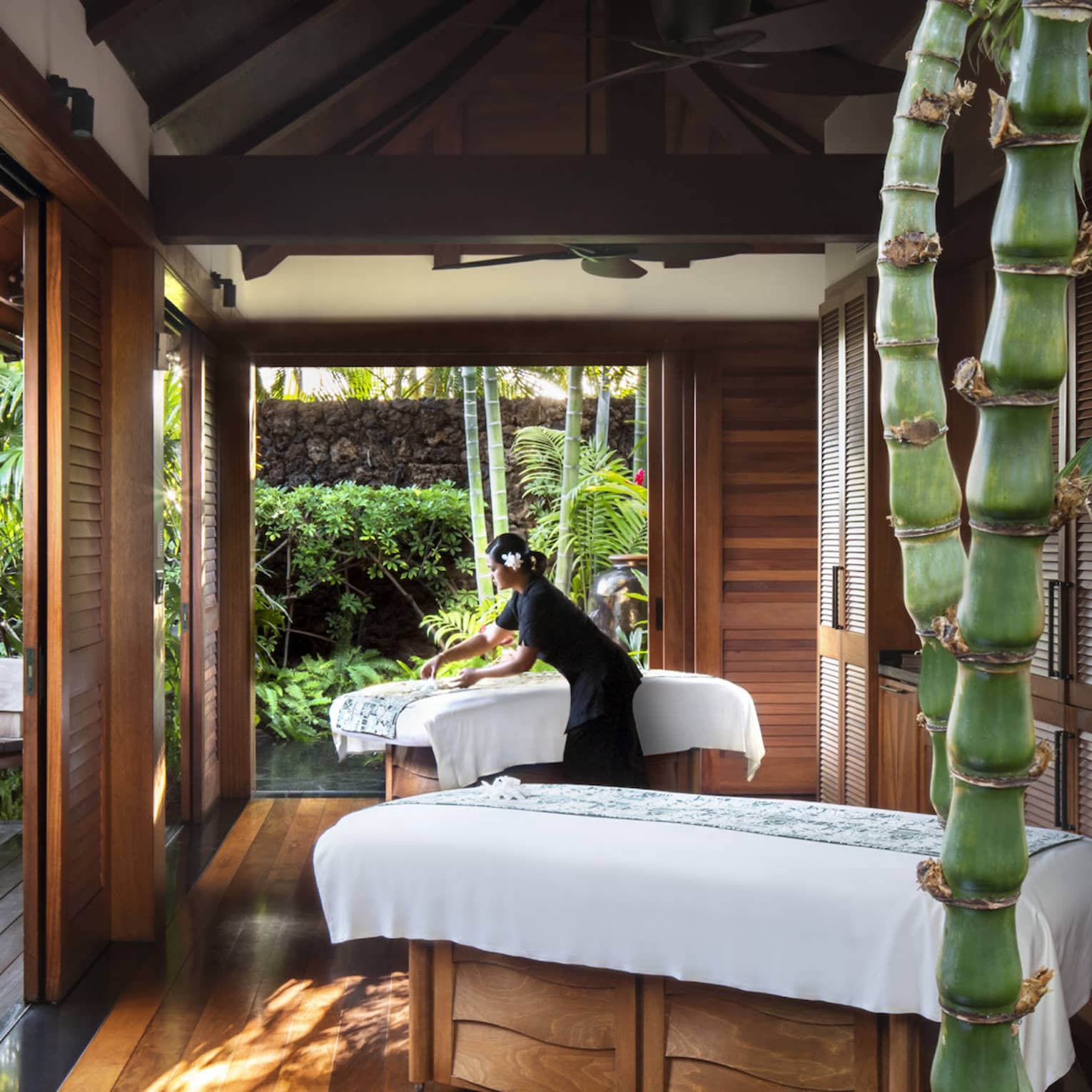 Spa staff spreads sheet on couples massage beds on open-air pavilion 